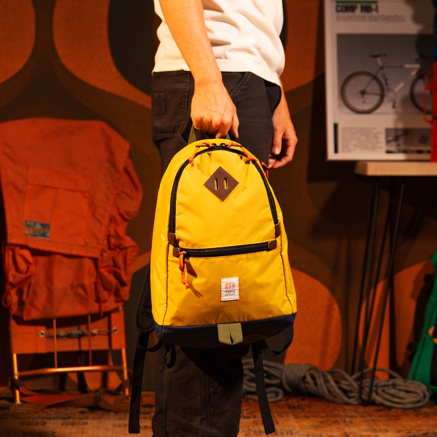 General model view of Topo Designs Classic Teardrop Backpack in "Yellow / Midnight" being held by top handle.