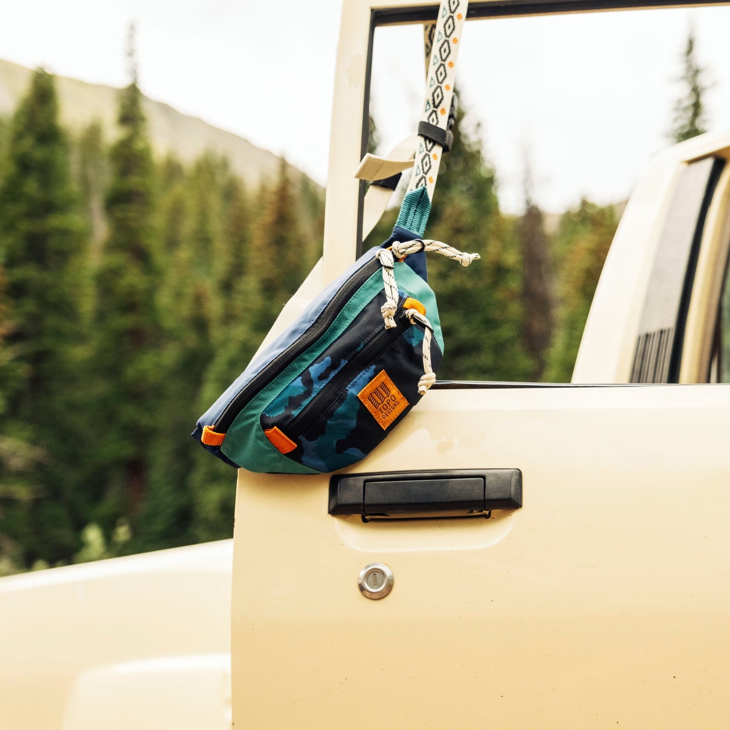 Teal and black waist pack with orange accents hanging from rope on vehicle window.