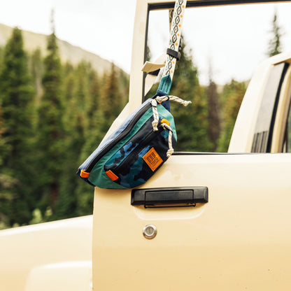 Teal and black waist pack with orange accents hanging from rope on vehicle window.
