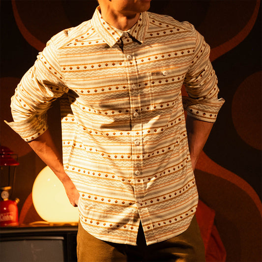 General lifestyle image of person wearing a "Bone White Sunset Stripe" Mountain Shirt Lightweight with a dark background with a warm glow in a dimly lit room.
